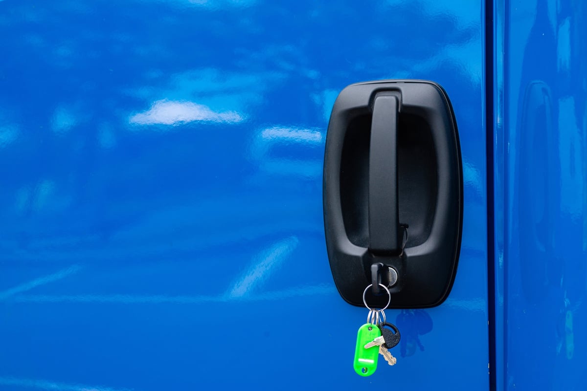 Close up of car keys with a bright green keychain inserted into a blue vehicle door lock
